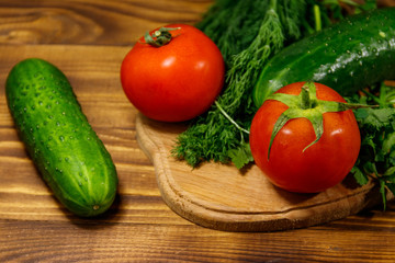 Fresh tomatoes, cucumbers, parsley and dill on cutting board on wooden table