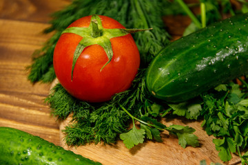 Fresh tomatoes, cucumbers, parsley and dill on cutting board on wooden table