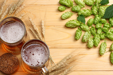 Glass beer with hop cones and wheat ears on light wooden background. Beer brewery concept. Beer background. top view