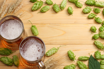 Glass beer with hop cones and wheat ears on light wooden background. Beer brewery concept. Beer background. top view