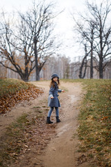 Obraz premium A cute girl in gey coat and gray hat in the oak wood in autumn walking at the sunset