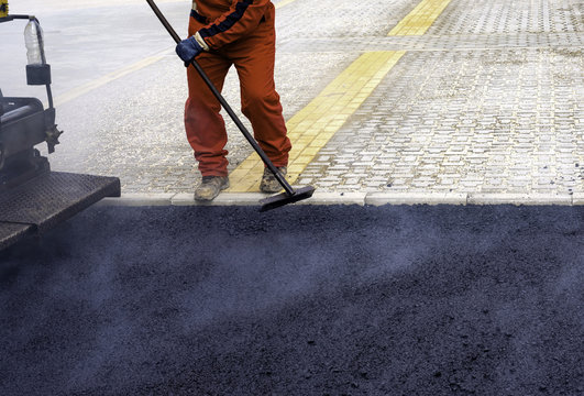Worker distributes on the edge the asphalt laid out for the construction of a road