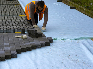 Construction worker laying interlocking paving concrete onto sheet nonwoven bedding sand and...