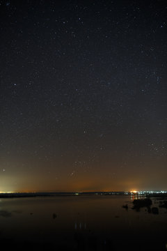 Bright stars of the night sky against the background of the smooth surface of the lake.