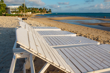 Four white wooden sun beds on the sandy beach