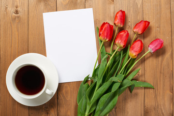 tulips are on wooden boards, cup of coffee, blank paper sheet with place for text - holiday and greeting concept