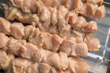 raw chicken breast meat coated with a marinade and onion, strung on skewers, a shish kebab preparation