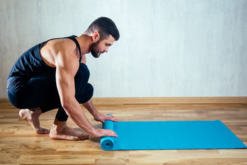 The man's hand spreads the yoga mat on the floor. blue yoga mat