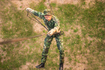 Soldier training rappel with rope. Military man does hanging on climbing equipment.