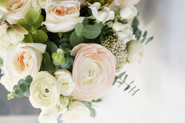 Wedding bouquet of white roses and buttercup on a wooden table. Lots of greenery, modern asymmetrical disheveled bridal bunch
