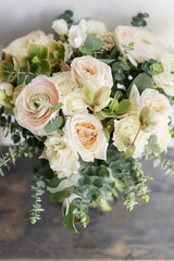 Wedding bouquet of white roses and buttercup on a wooden table. Lots of greenery, modern asymmetrical disheveled bridal bunch