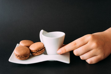 Woman taking set of cup of coffee and macarons against black ba