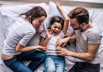 The happy daughter and parents joying on the bed