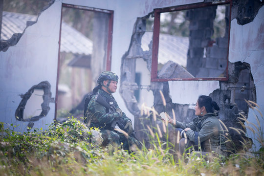 Female Journalist Interview Soldier During War Conflict. Photojournalist  Work On Grass Field Concept.