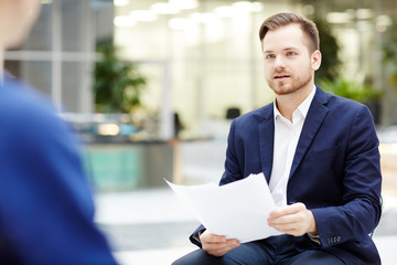 Fototapeta premium Young businessman with documents sitting and communicating with colleague