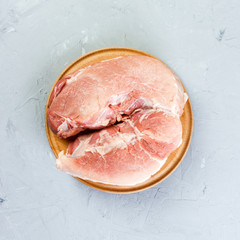fresh large piece of pork on a round wooden cutting board. Top view on grey background