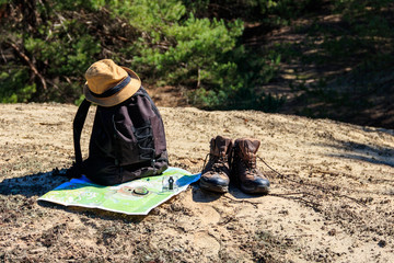 Tourist backpack with hiking boots, hat, compass and map on the glade in pine forest