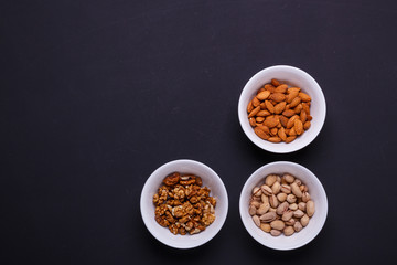 Three bowls with different nuts on a black table