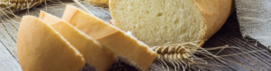 Banner of Sliced bread with wheat spikes on wooden table closeup