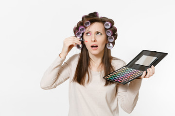 Fun young woman with curlers on hair with palette colorful eyeshadows isolated on white background....