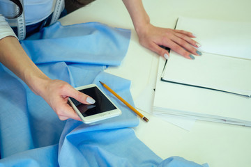 the seamstress holds the phone in her hand. the tailor sews on the sewing machine. dressmaker types the text on the phone