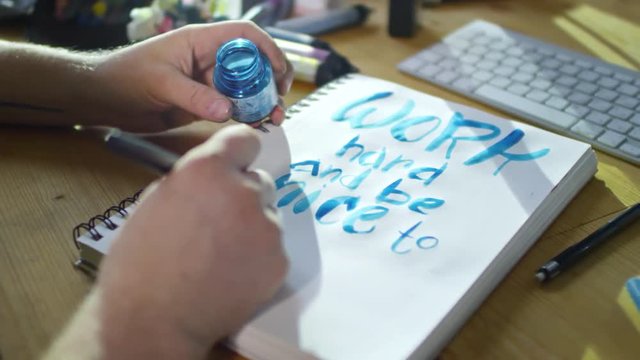 Close up shot of unrecognizable illustrator creating poster with inspirational quote saying Work Hard and Be Nice to People