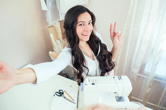 beautiful woman seamstress with long hair does selfie. tailor creates a collection of clothes on the background of a sewing machine. concept of online sewing education