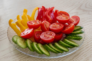 Slices of tomatoes, cucumbers and peppers served on a plate on white table .