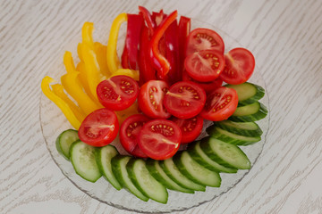 Slices of tomatoes, cucumbers and peppers served on a plate on white table . Top view.