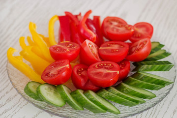 Slices of tomatoes, cucumbers and peppers served on a plate on white table .