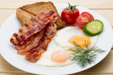Fried eggs with bacon on the wooden table.