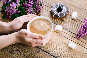 coffee in hand, a wooden table, a lilac and a donut, a spring day
