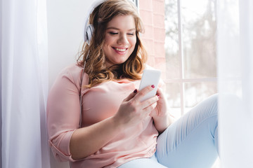 young smiling woman in headphones using smartphone at home