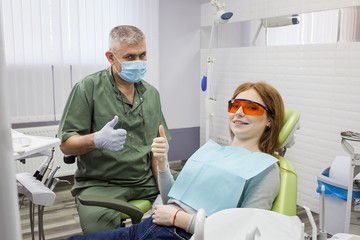 Woman and dentist showing thumb up sign at office (clinic)