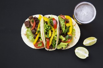 Mexican tacos with beef and vegetables, beer and lime on a black background, top view. Copy space....