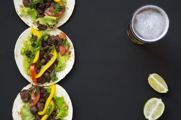 Mexican tacos with beef and vegetables, beer and lime on a black background, top view. Copy space. Flat lay.