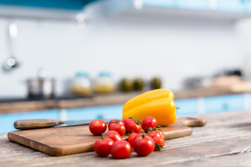 selective focus of fresh cherry tomatoes and bell pepper on tabletop with wooden cutting board and...