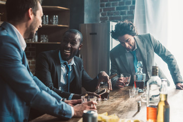 cheerful male friends laughing and drinking whiskey together