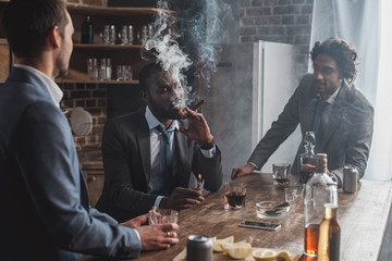 young multiethnic businessmen talking while smoking cigars and drinking whiskey