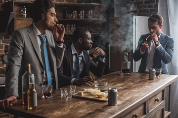 young multiethnic businessmen smoking cigars and drinking alcohol while partying together