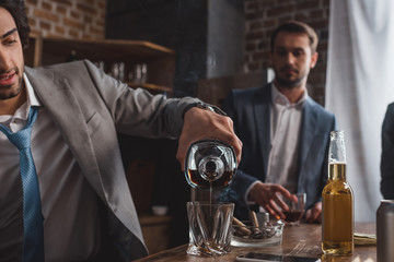 cropped shot of man in suit pouring whiskey while friend standing behind