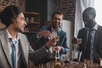 smiling multiethnic male friends in suits drinking tequila together - Powered by Adobe