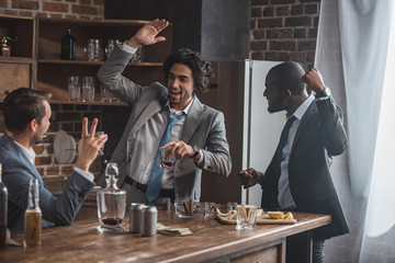 cheerful multiethnic businessmen drinking whiskey and partying together