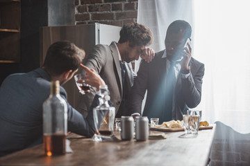 multiethnic men in suits drinking alcohol and talking by smartphone