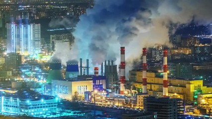 Zoom in on power plant emitting smoke from smokestacks over night city skyline. 4K UHD Timelapse. 