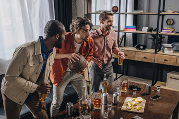 side view of multiethnic men playing with basketball ball and drinking beer together