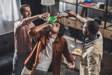 high angle view of man drinking from funnel while friends pouring alcohol beverages from glass bottle and can