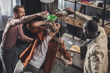  hoge hoekmening van man die uit de trechter drinkt terwijl vrienden alcoholische dranken schenken © LIGHTFIELD STUDIOS
