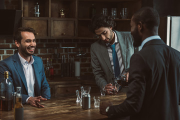 male friends in suits smiling each other, talking and drinking alcoholic beverages during stag party