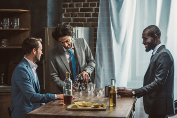 three smiling young multiethnic men in suits drinking alcohol beverages together